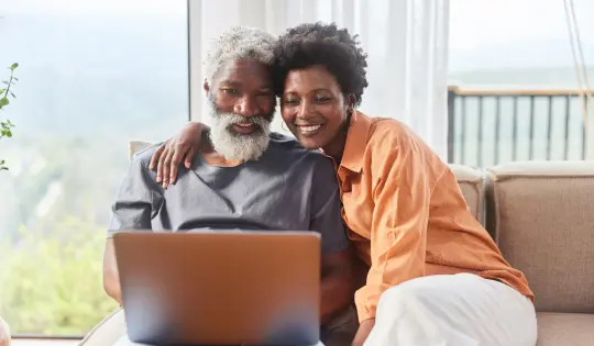 older couple sitting on couch looking at a laptop and smiling for some reason